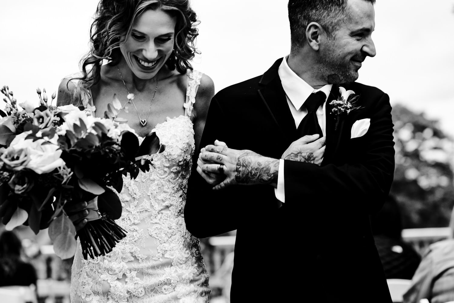 A candid black and white picture of a bride and groom holding hands and smiling together moments after their wedding ceremony at Longview Mansion in Kansas City. 