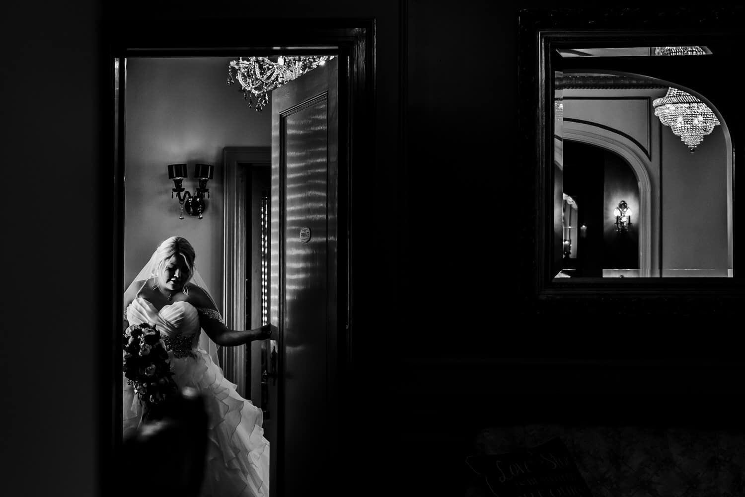 A bold, black and white image of a bride opening the door of her bridal suite to walk down the aisle on her 2020 wedding day at The DeLeon in Kansas City. 