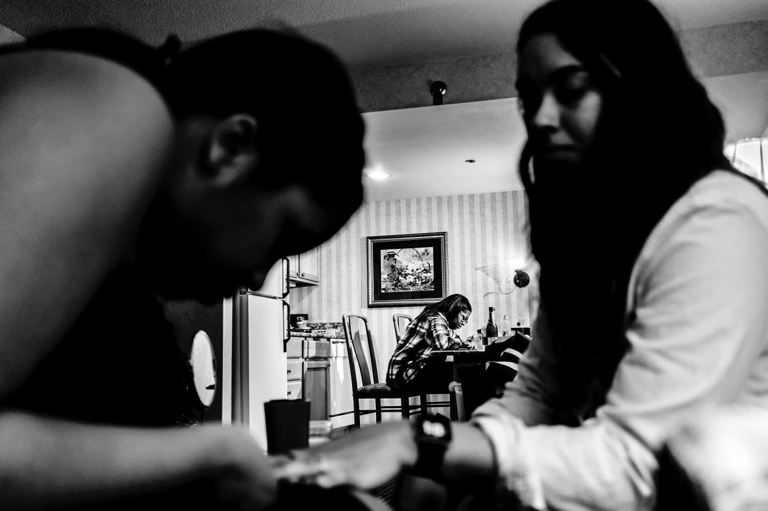A candid black and white picture of a woman getting her nails painted in the foreground, with another woman hunched over a table writing something in the background on the morning of a rainy winter wedding at The Station in Kansas City. 