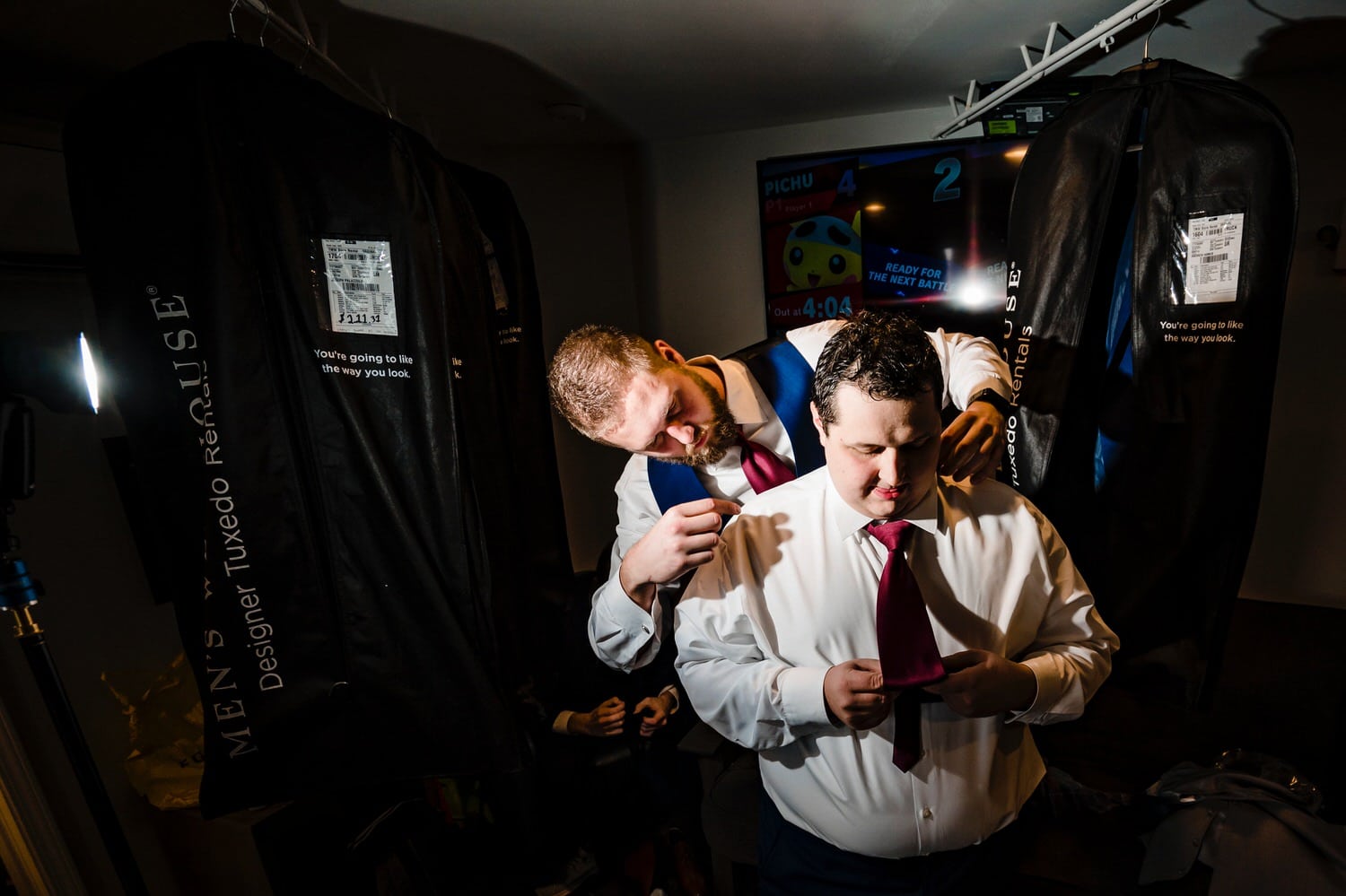 A colorful candid picture of a groom's best man helping tie his tie on the morning of a rainy winter wedding at The Station in Kansas City. 