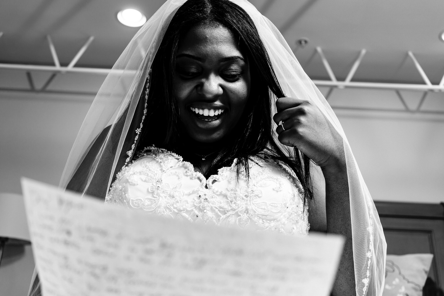 A candid black and white picture taken from the ground looking up of a bride laughing with glee as she reads a letter from her groom on the afternoon of her winter wedding at The Station in Kansas City. 