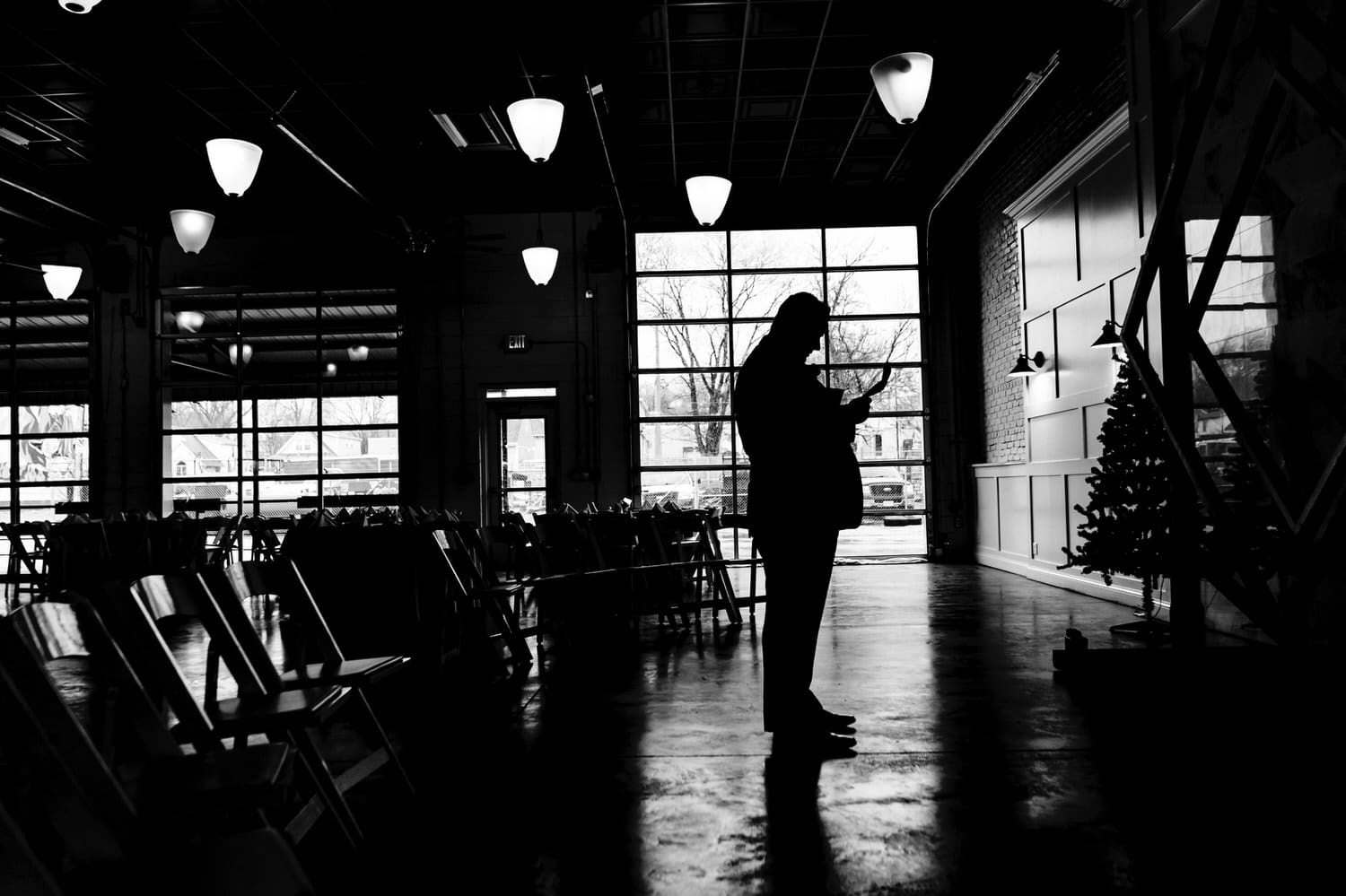 A dramatic black and white, silhouetted picture of a groom reading a letter from his bride on the afternoon of a rainy winter wedding in Kansas City at The Station. 