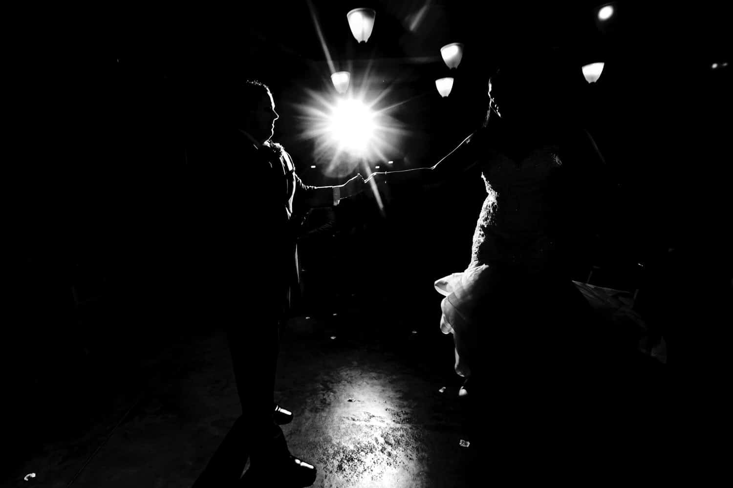 A dramatic, black and white, almost silhouetted picture of a groom twirling his bride on the dance floor as they share their first dance on their rainy winter wedding day at The Station in Kansas City. 