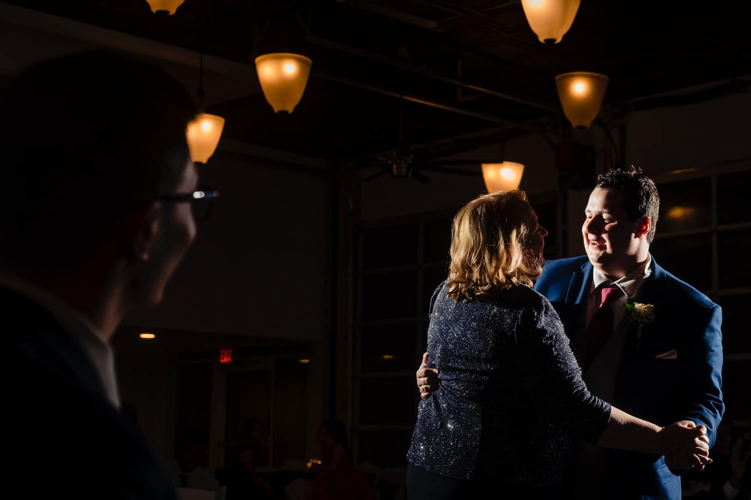 A colorful, candid picture of a groom dancing with his mom as his brother looks on during his winter wedding reception at The Station in Kansas City. 