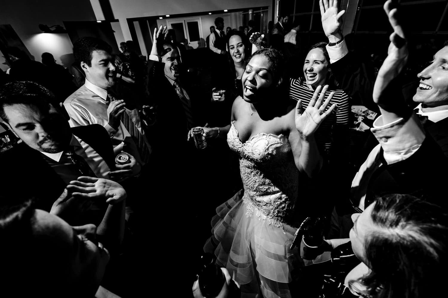 A black and white, candid picture of a bride and groom in the middle of the dance floor, surrounded by friends and family during their winter wedding reception at The Station in Kansas City. 