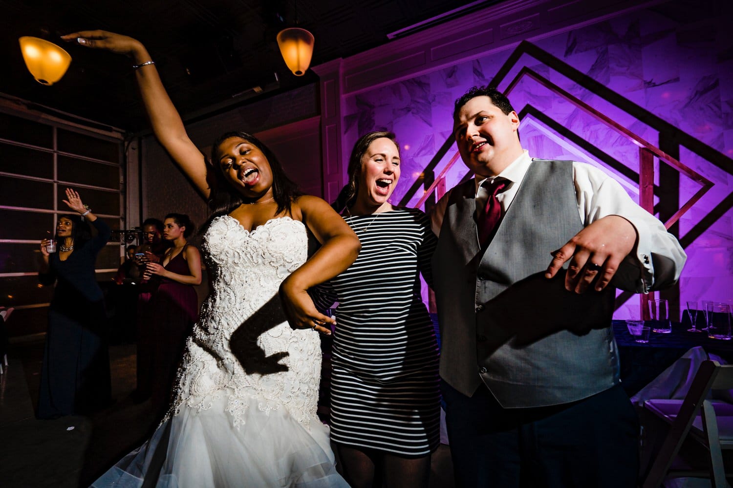 A colorful, candid picture of a bride and groom in the middle of the dance floor, surrounded by friends and family during their winter wedding reception at The Station in Kansas City. 