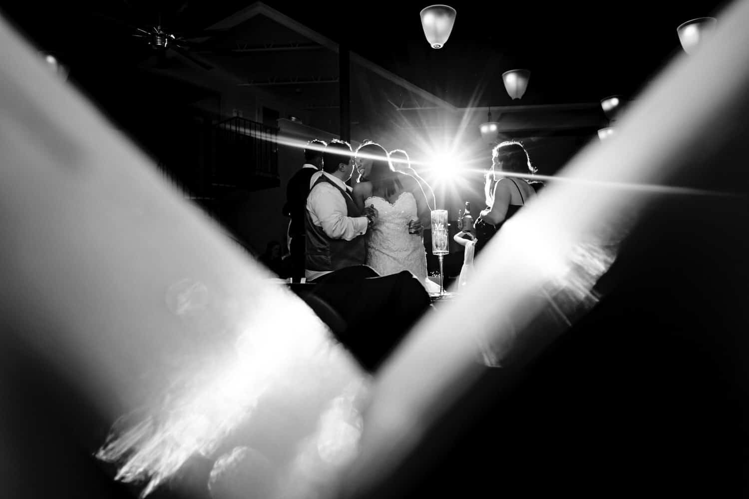 A black and white, candid picture of a bride and groom in the middle of the dance floor, surrounded by friends and family during their winter wedding reception at The Station in Kansas City. 
