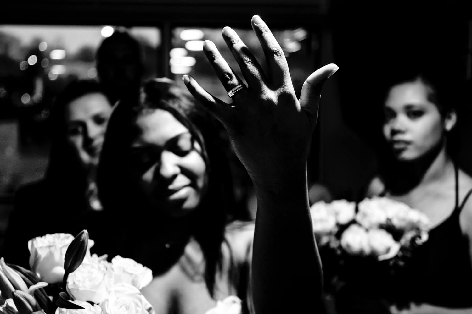 A dramatic, candid, black and white picture of a bride throwing her left hand up in the air to show off her new wedding band as she dances to Beyonce, her sisters and bridesmaids visible in the background on her rainy winter wedding day in Kansas City. 