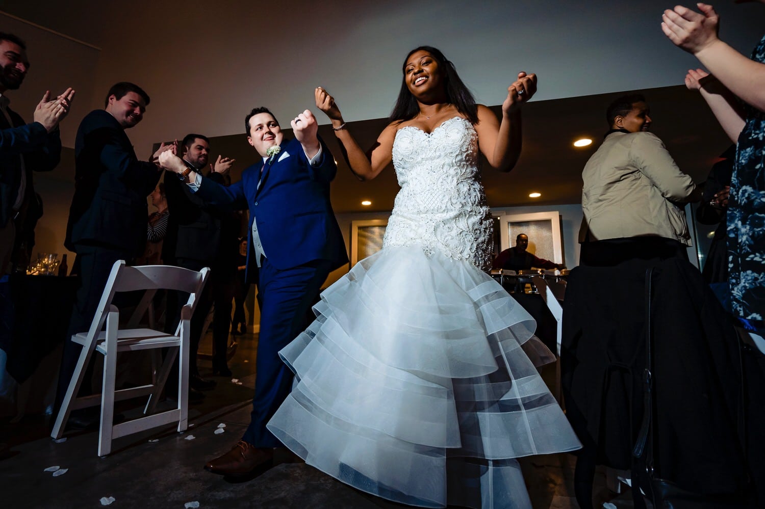 A colorful, candid picture of a bride and groom celebrating and dancing as they enter their reception on a rainy winter wedding day at The Station in Kansas City. 