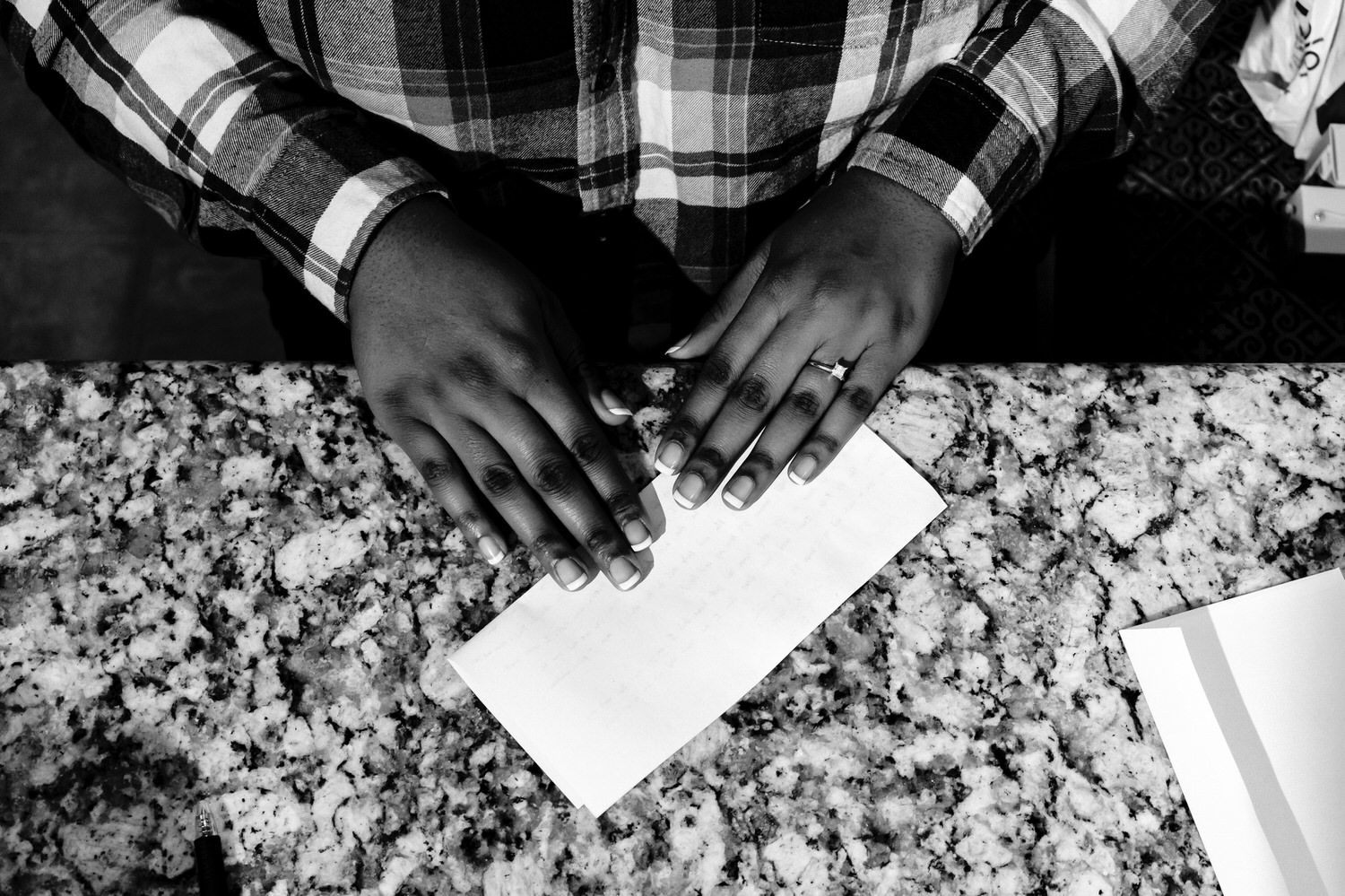 An up-close black and white picture of an African American woman folding a piece of paper in half, the focus on her engagement ring on the morning of her wedding at The Station in Kansas City. 