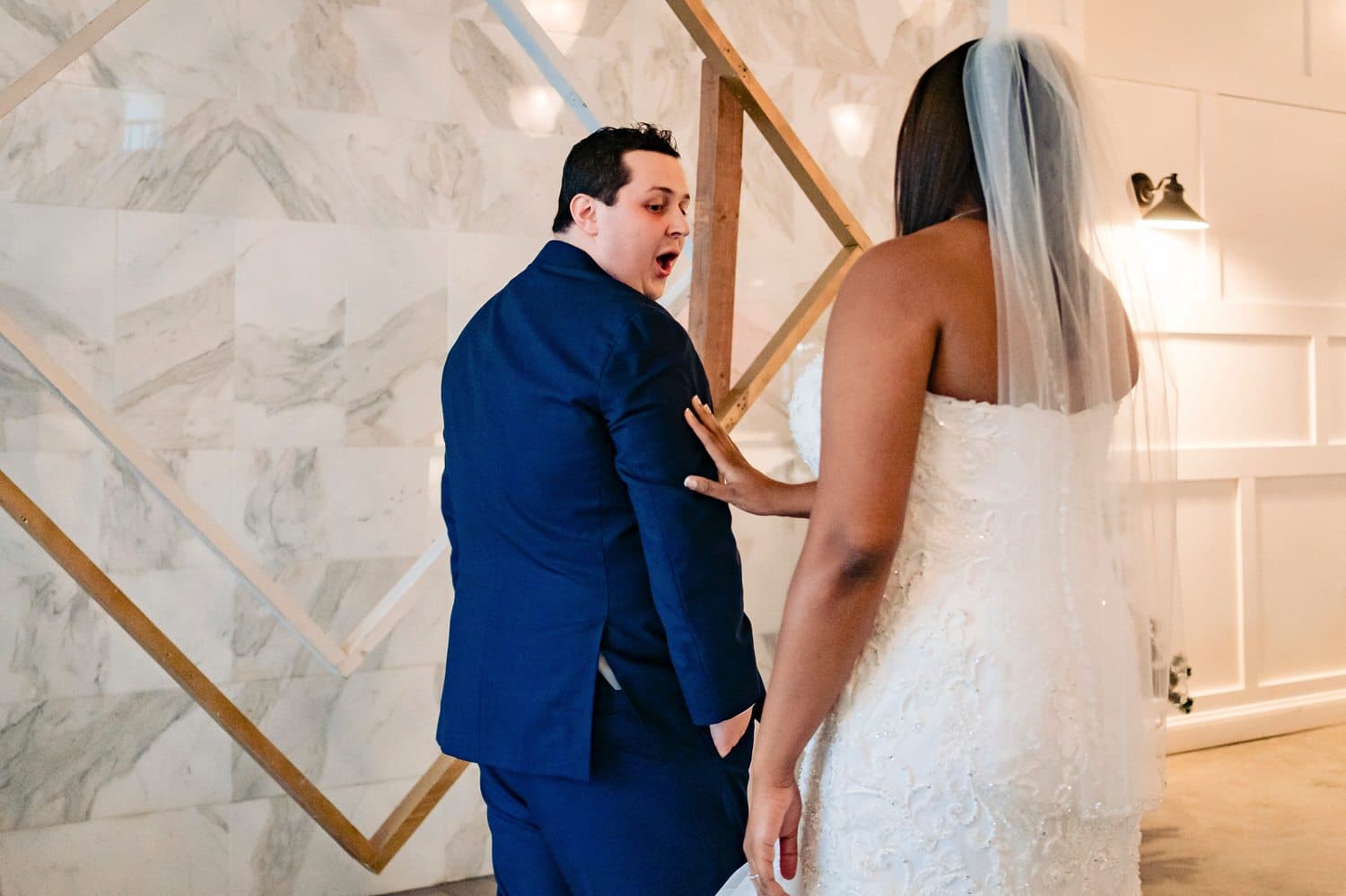 A colorful, candid picture of a groom turning around in surprise as his bride taps him on the shoulder during their first look on their rainy winter wedding day at The Station in Kansas City. 