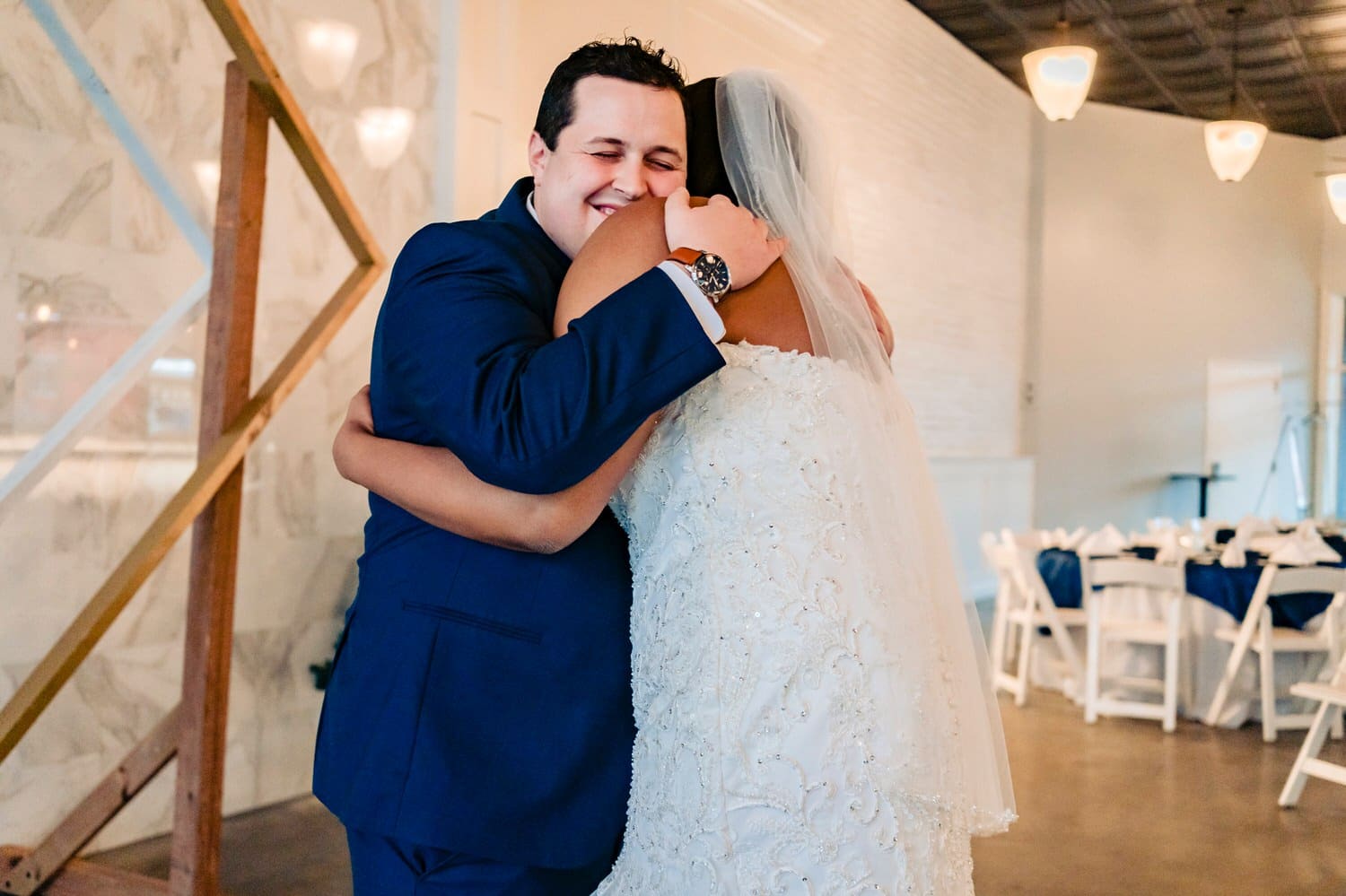 A colorful, candid picture of a groom in a blue suit giving his bride a big hug moments after their first look on their winter wedding day in Kansas City at The Station. 