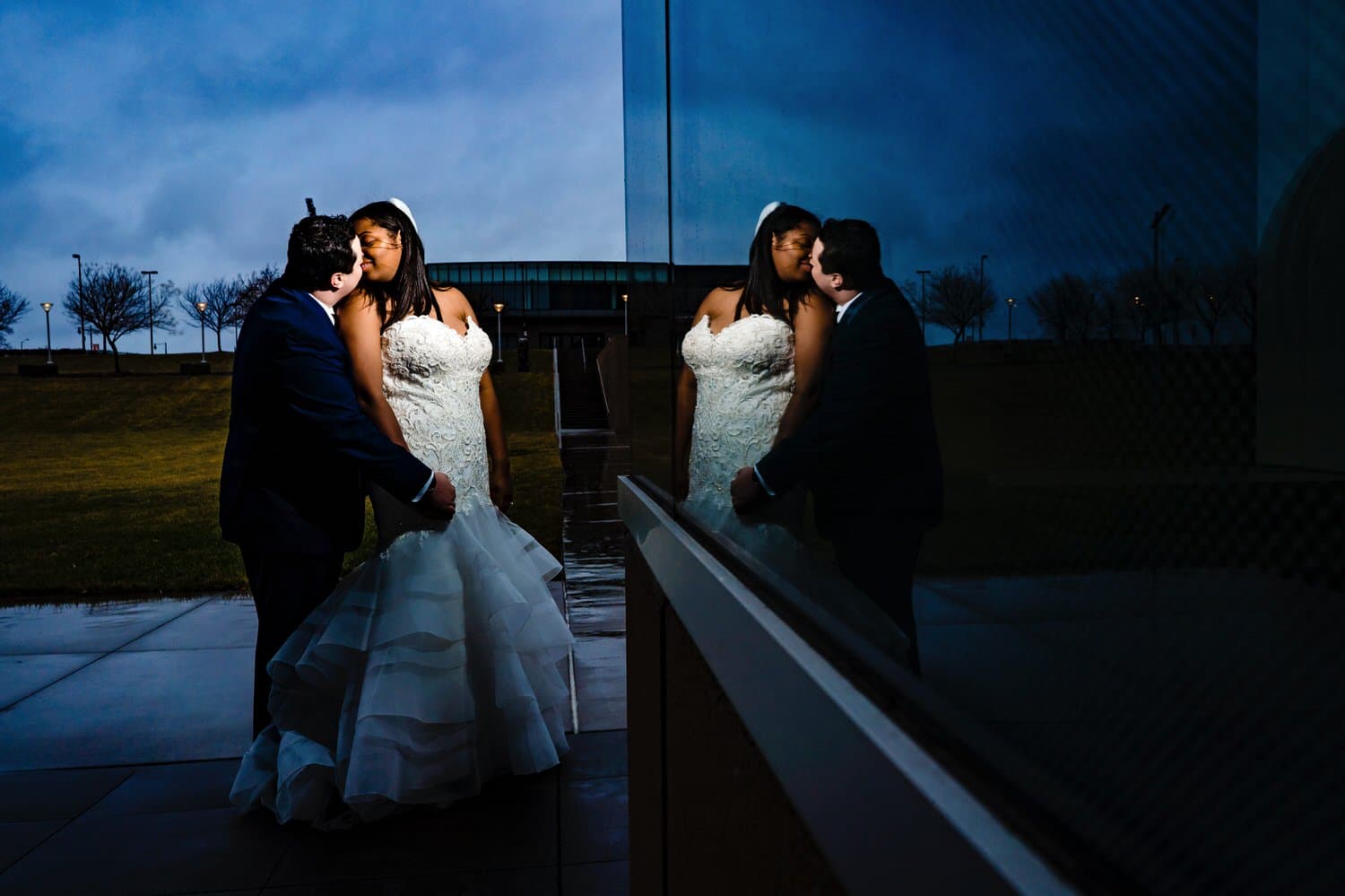 A colorful, dramatic picture with a reflection of a bride and groom leaning in to share a kiss on their rainy winter wedding day in Kansas City. 