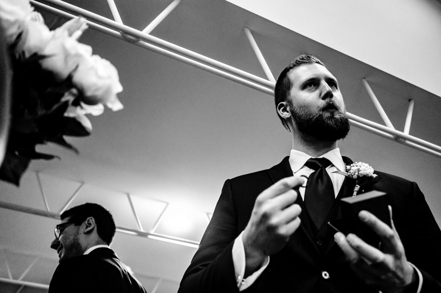 A candid black and white picture of a best man holding up a wedding band and whistling moments before a wedding ceremony at The Station on a rainy winter day in Kansas City. 