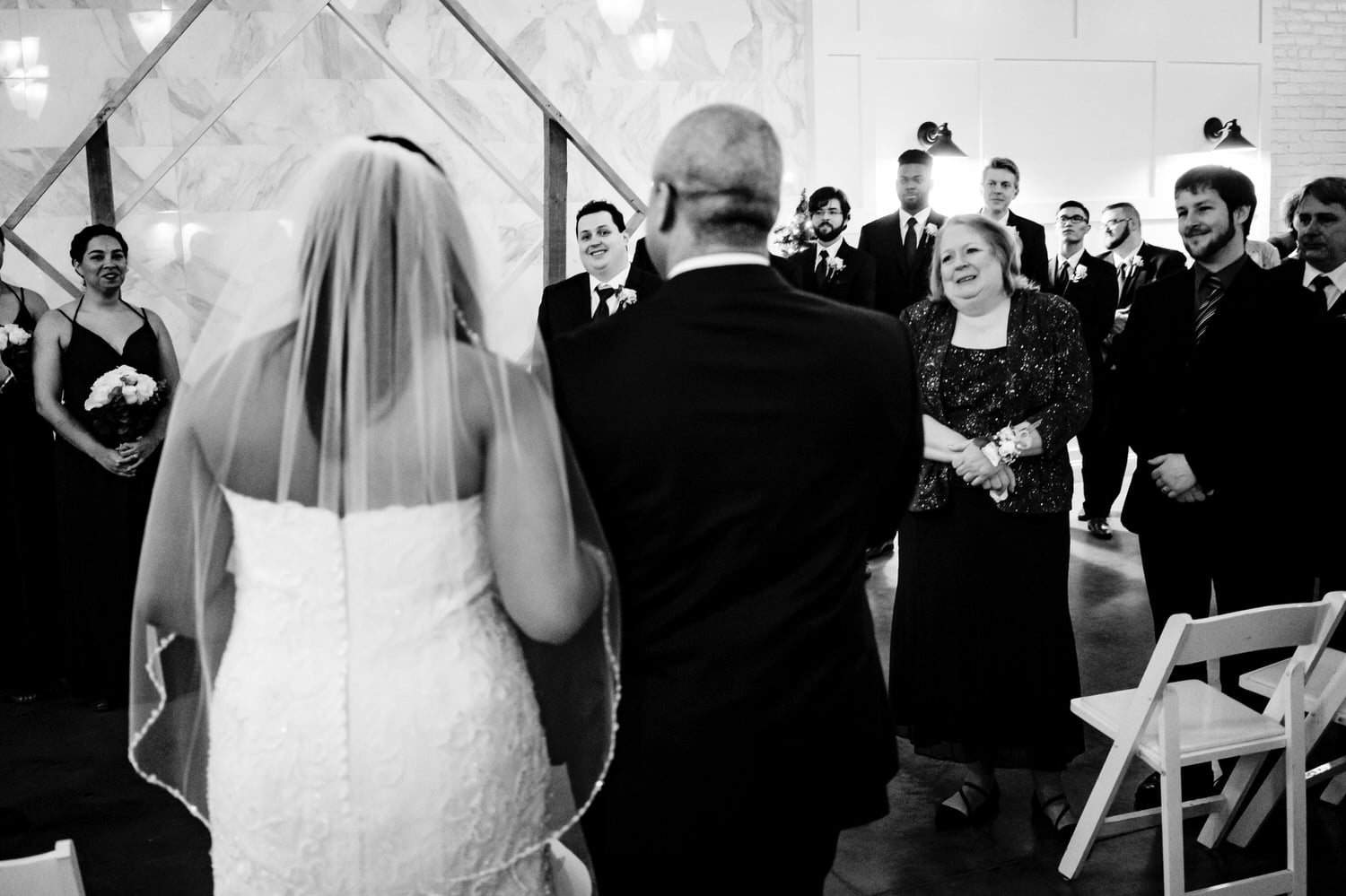 A candid black and white picture taken over the shoulder of the bride and her father as they approach her groom during a winter wedding ceremony at The Station in Kansas City. 