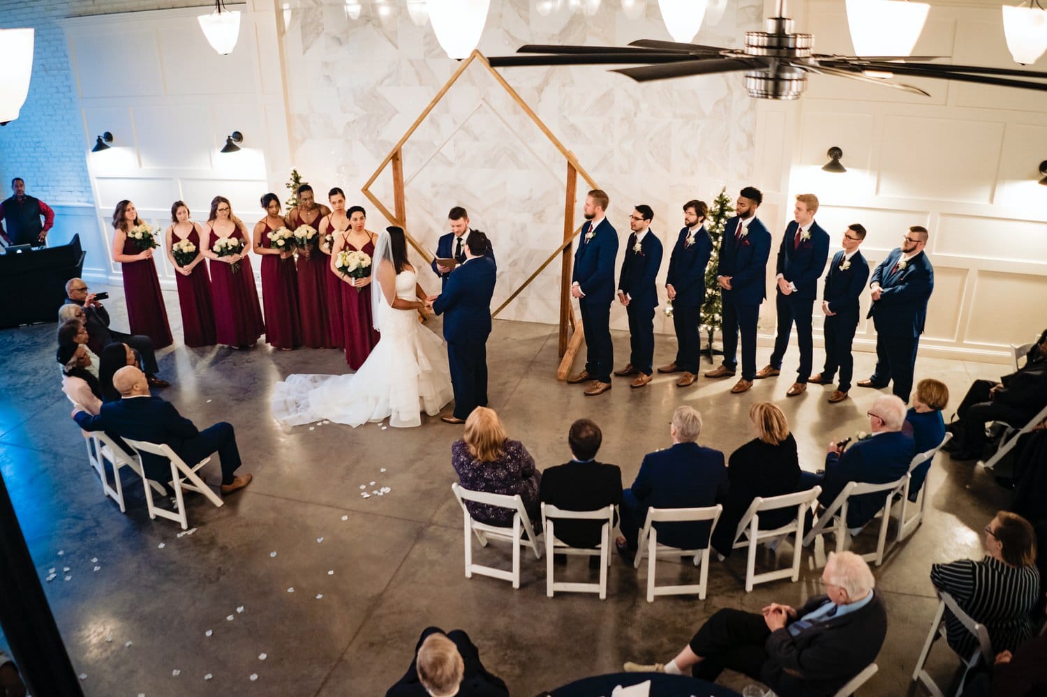A colorful, candid picture taken from above of a bride and groom exchanging their vows as their family and friends watch-on during a winter wedding at The Station in Kansas City. 