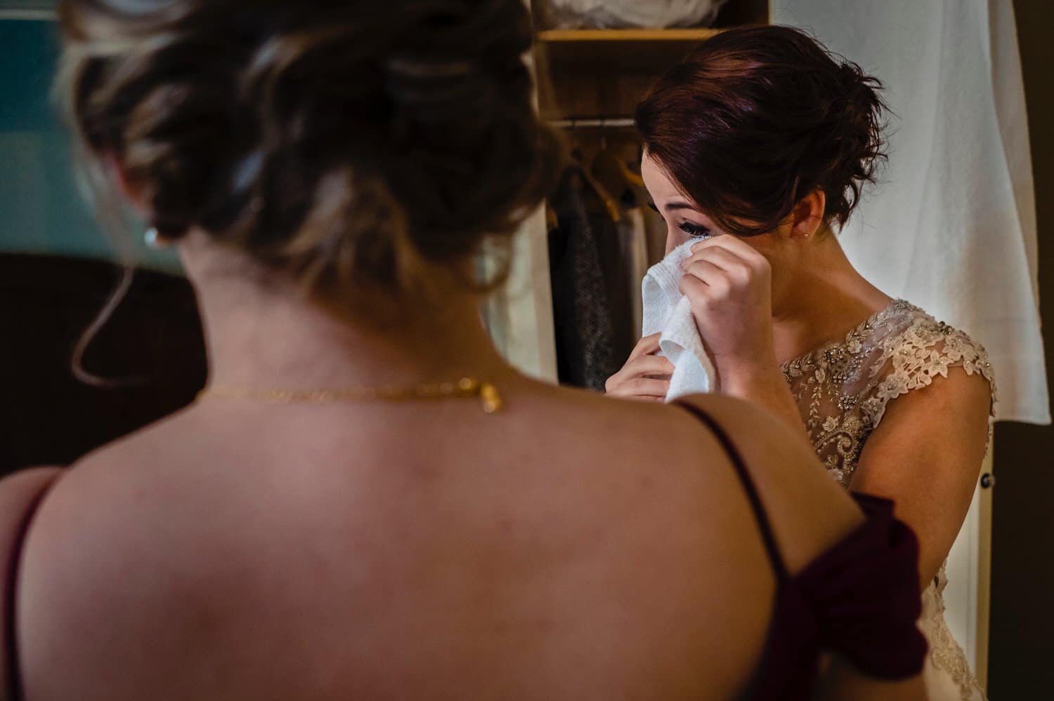 A colorful, candid picture of a bride wiping tears from her eyes as her sister watches on the afternoon of a winter wedding at The Elms. 