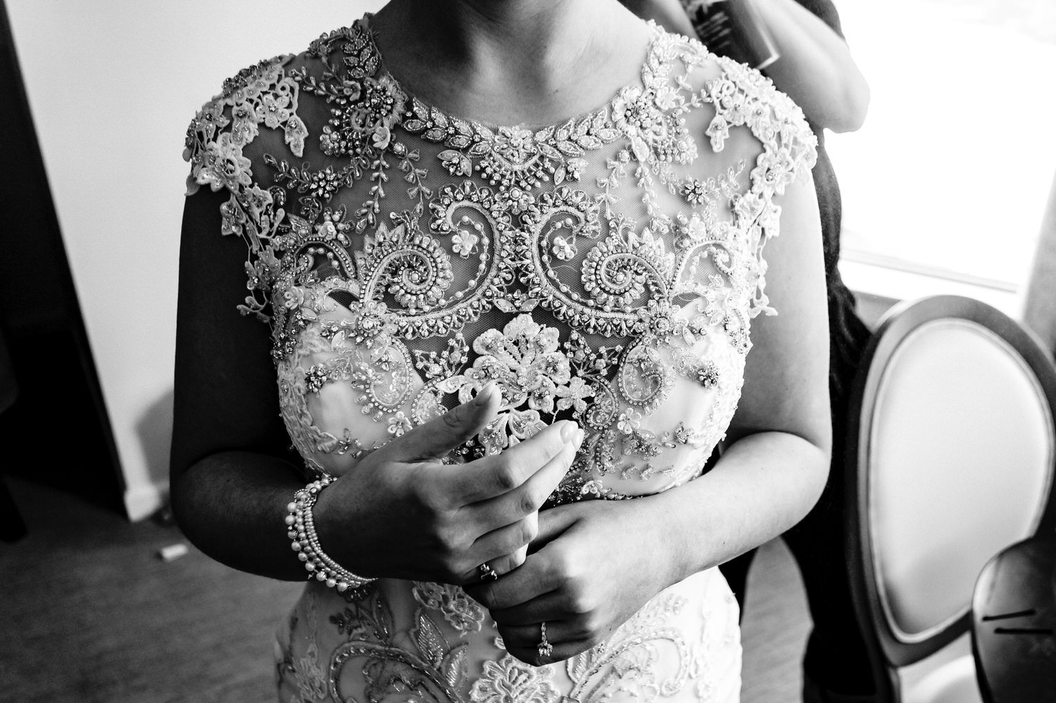 A black and white picture of a bride in a beaded gown ringing her hands and playing with the rings on her fingers as a hair stylist puts her veil in on a wedding day at The Elms. 