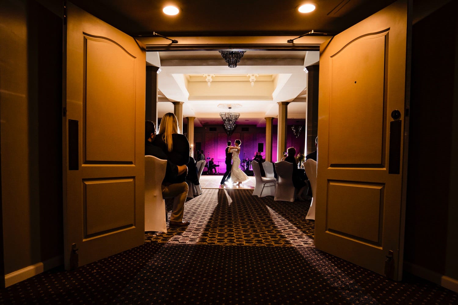 A colorful, candid picture taken through the open doors of a ballroom at The Elms of a bride and groom gracefully waltzing across the dance floor for their first dance. 