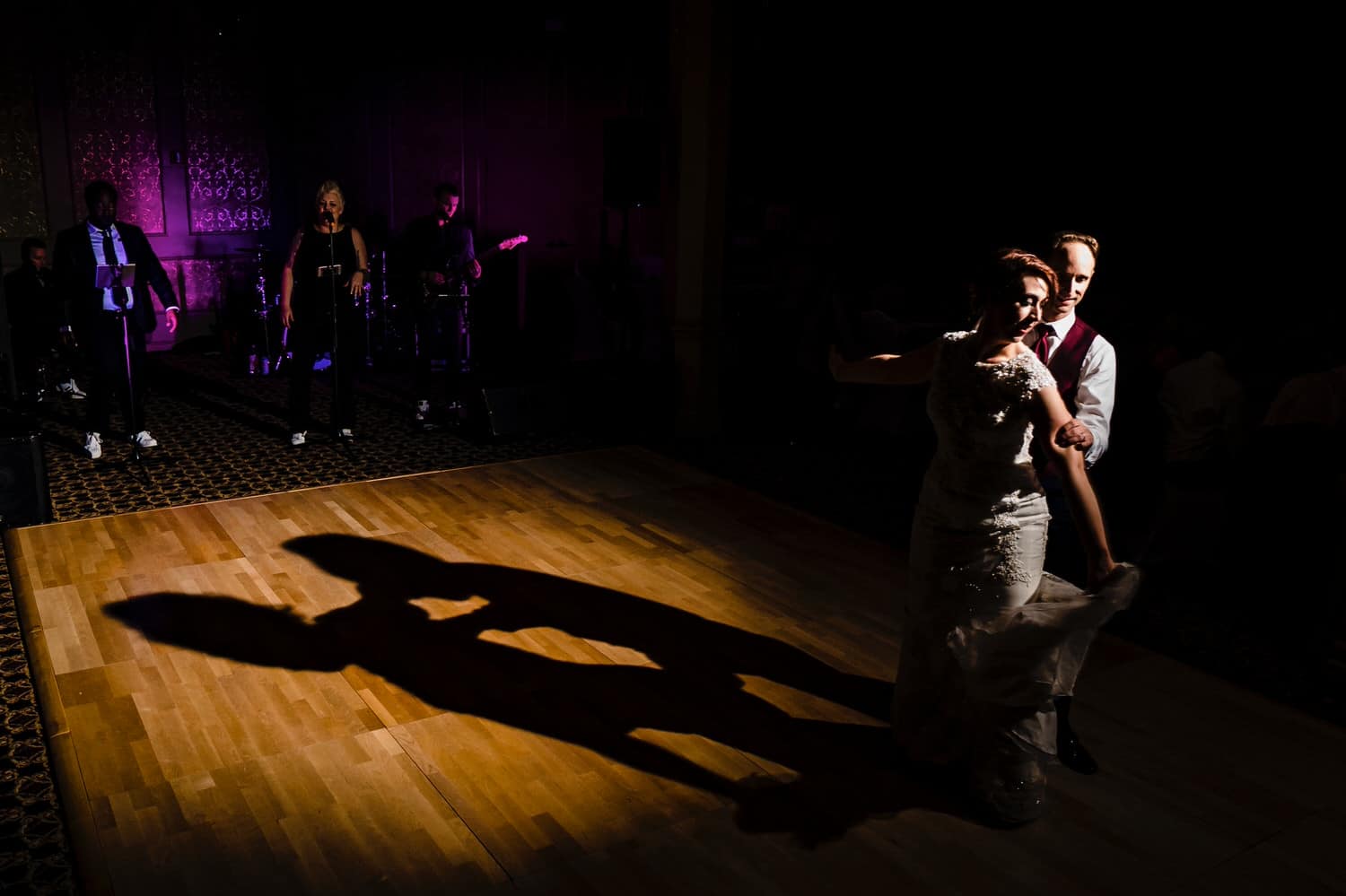 A bold picture of a bride and groom gracefully dancing across a dance floor, their shadow visible on the floor behind them during their wedding reception at The Elms. 