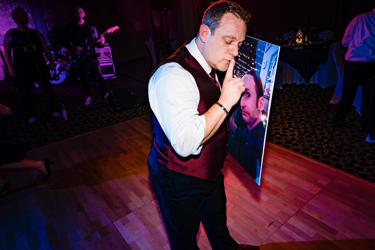 A close-up, candid picture of a groomsman dancing intimately with a printed picture of the groom during a wedding reception. 