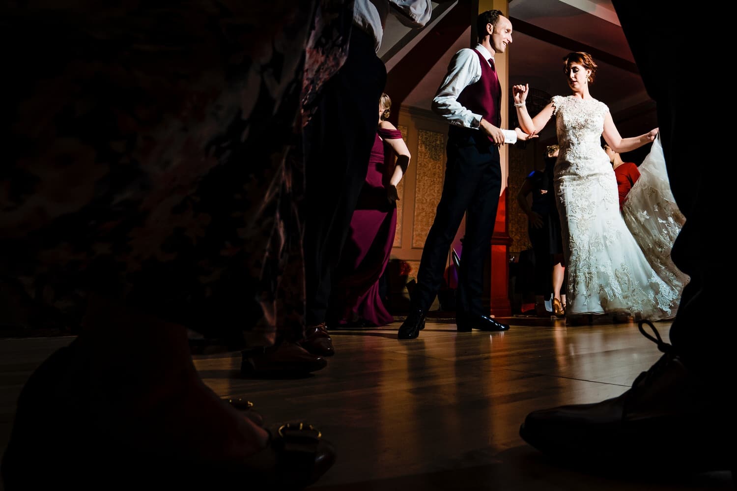 A candid picture taken through the legs of dancers of a bride and groom spotlit in the middle of the dance floor during their wedding reception at The Elms. 