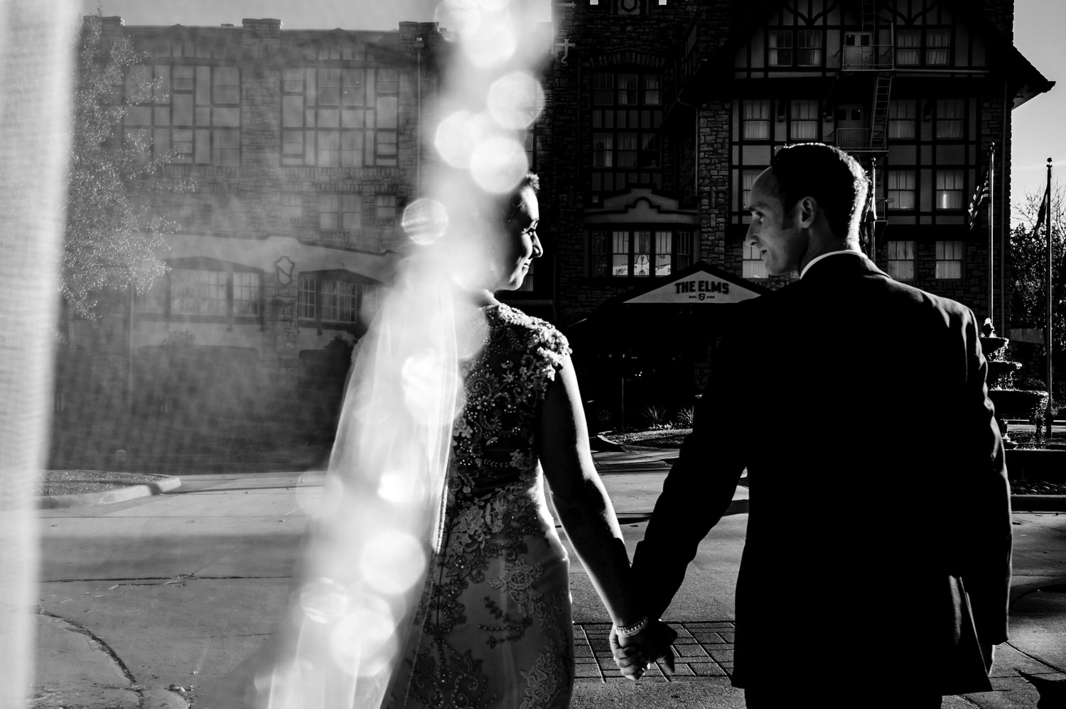 A dramatic black and white picture taken from beneath a bride's veil of a bride and groom walking hand in hand towards The Elms on their winter wedding day. 
