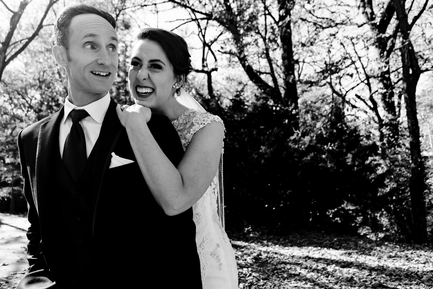 A candid black and white picture of a bride leaning over her groom's shoulder, both of them laughing and smiling goofily on the afternoon of their winter wedding at The Elms. 