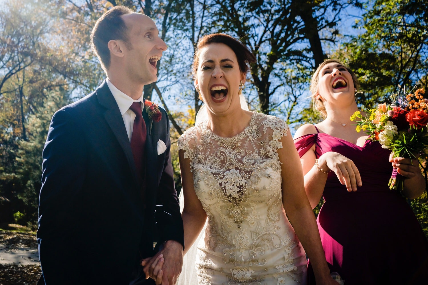 A vibrant, candid picture of a bride, groom, and bridesmaid laughing with their mouths wide open on a winter wedding day at The Elms. 