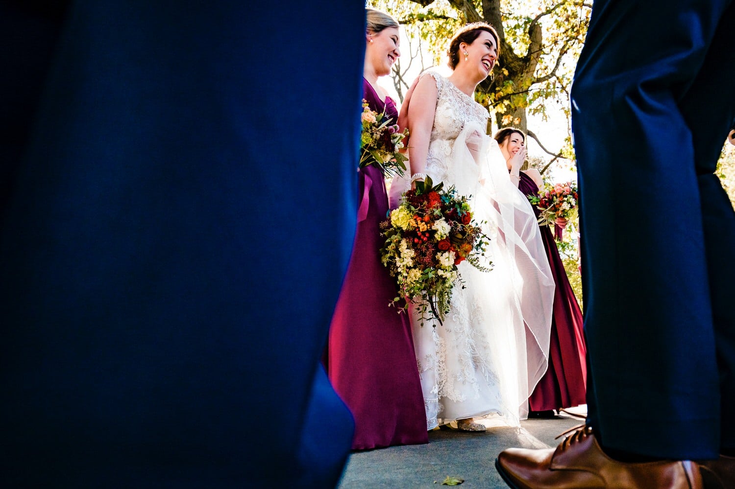 A colorful, candid picture taken between the legs of a group of groomsmen of a bride and her bridesmaids laughing hysterically. 