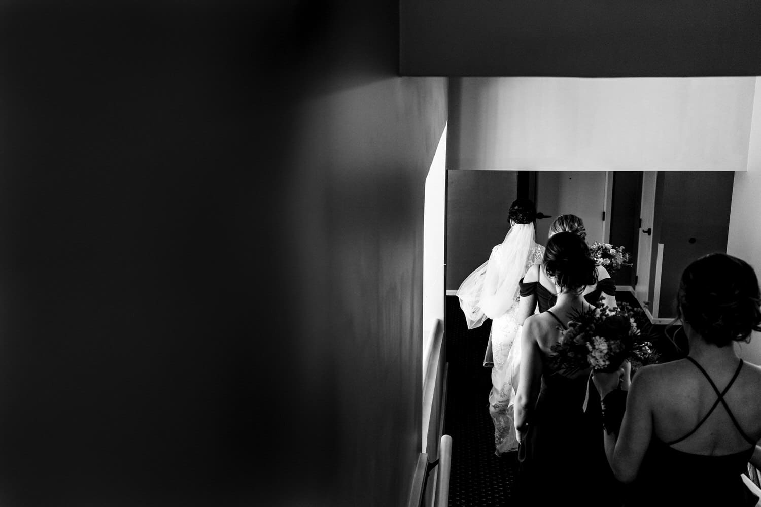 A candid black and white picture taken from behind a bride and group of bridesmaids as they make their way to the lobby of The Elms for a wedding ceremony. 