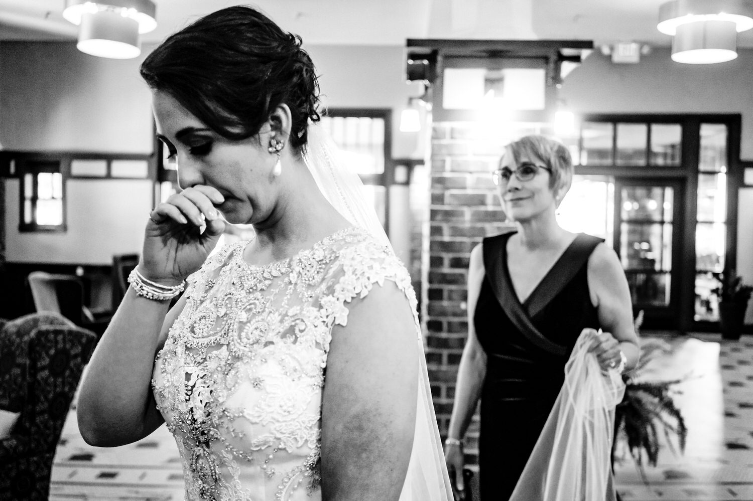 A candid black and white picture of a bride trying to hold back tears as her mom holds her veil, moments before walking down the aisle to get married. 