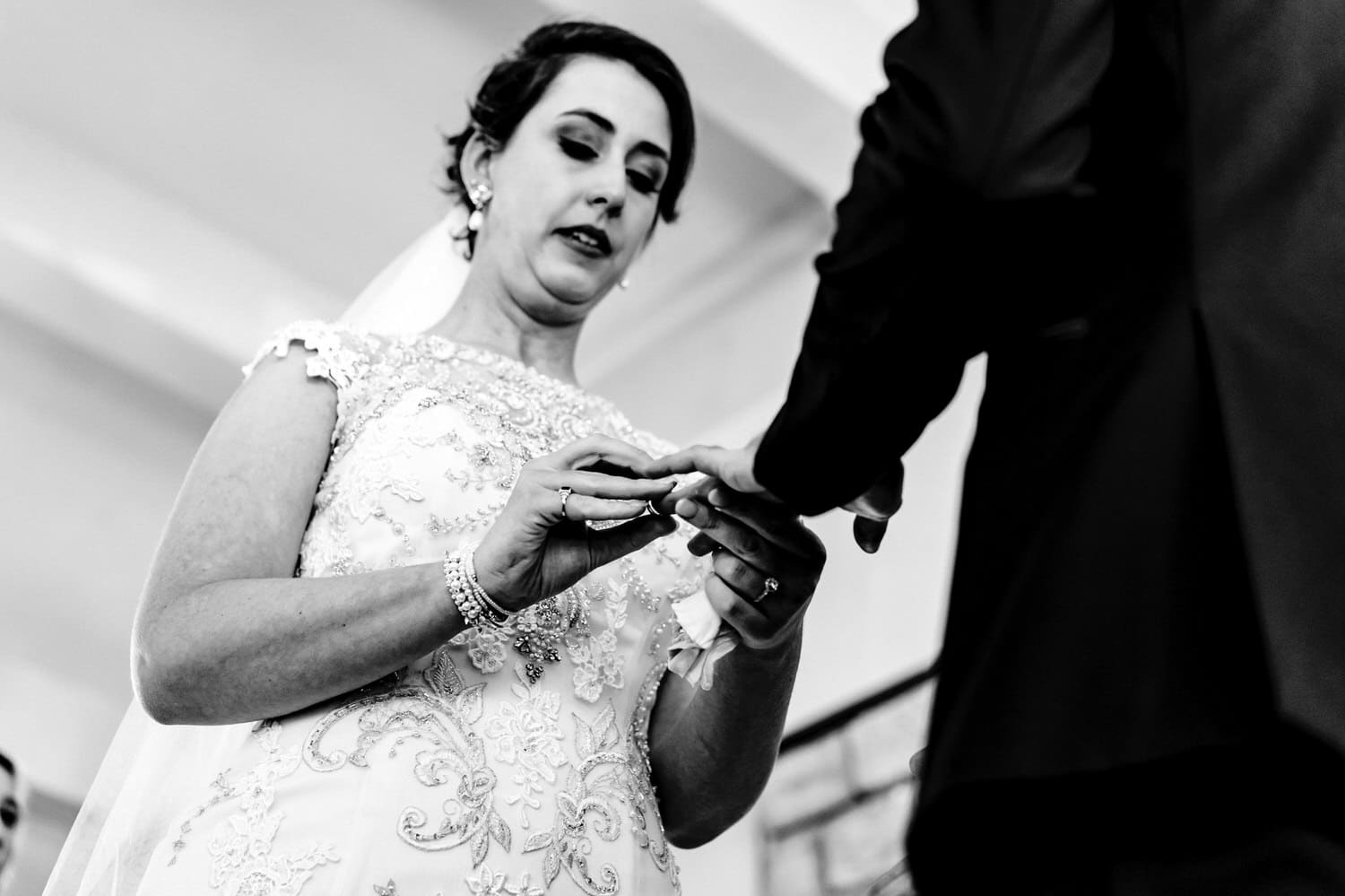 A candid black and white picture taken from the ground looking up of a bride putting a wedding band on her grooms' hand during their wedding ceremony at The Elms. 