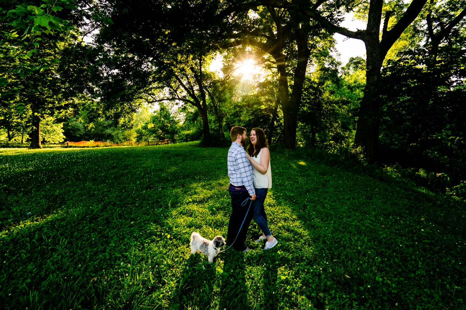 A colorful, candid picture of an engaged couple embracing and laughing together as their small dog sniffs the ground by their feet during their Kansas City Engagement Session. 
