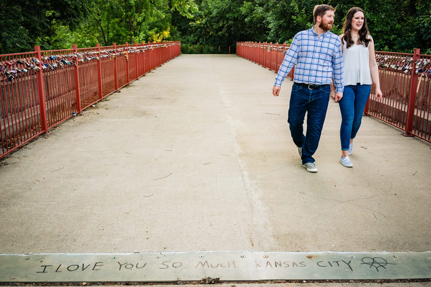A candid picture of an engaged couple holding hands walking across Kansas City Love Locks Bridge during their engagement session. 