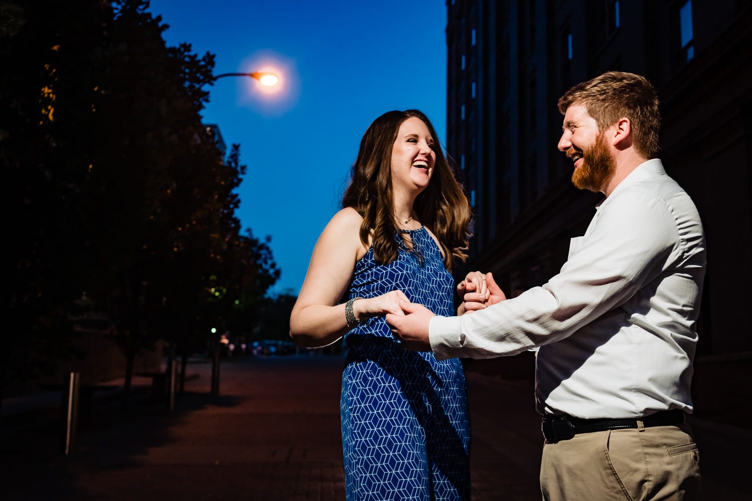 A colorful, candid picture of an engaged couple laughing together during their downtown Kansas City engagement session. 