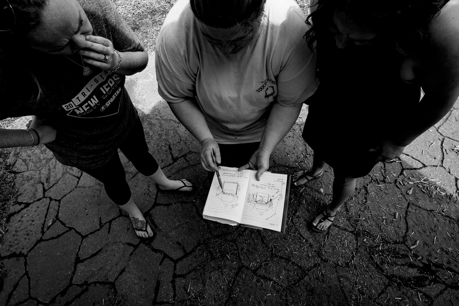 A black and white picture of three people standing around a notebook as one points out the plan on a wedding morning. 
