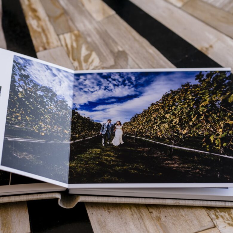 A picture of a wedding album laying open showing a couple walking hand-in-hand through a vineyard.