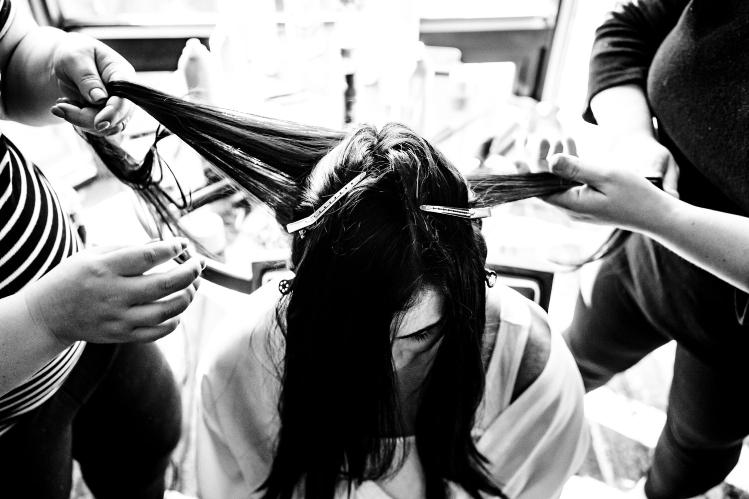 A black and white picture taken from the top looking down of a woman's hair getting pulled in two different directions by two different hairstylists on the day of her Kansas City Wedding. 