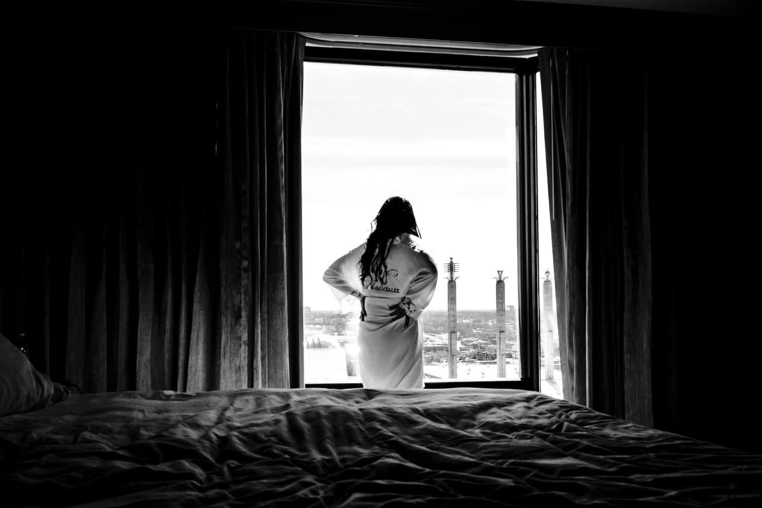 A candid black and white picture of a bride in a bride robe looking out over the downtown Kansas City skyline on the morning of her wedding. 