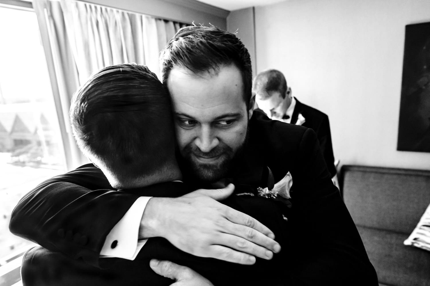 A black and white picture of a groomsman hugging a groom before sending him off for a first look with his bride. 