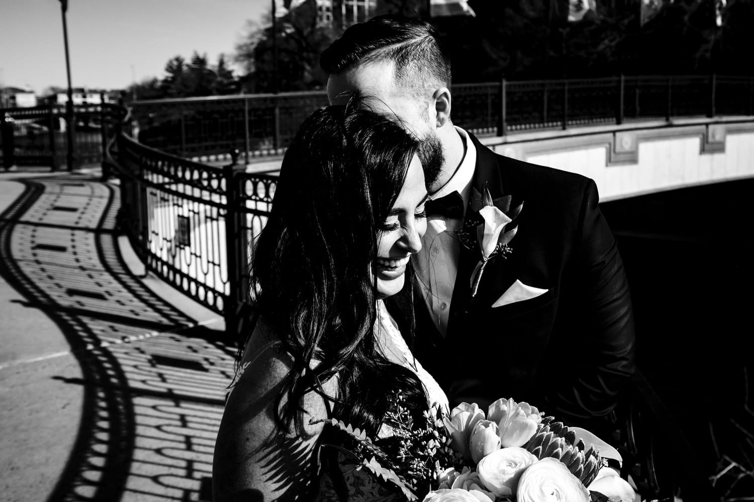 A close-up, candid, black and white picture of a bride and groom laughing together on a sunny winter wedding day in Kansas City. 