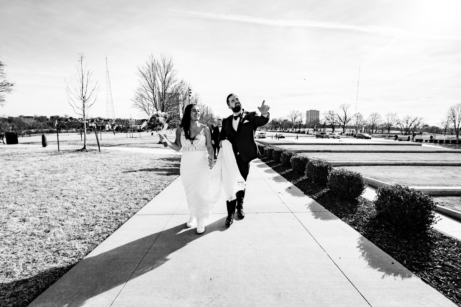 A candid black and white picture taken from a distance of a bride and groom laughing together as the groom points something out. 