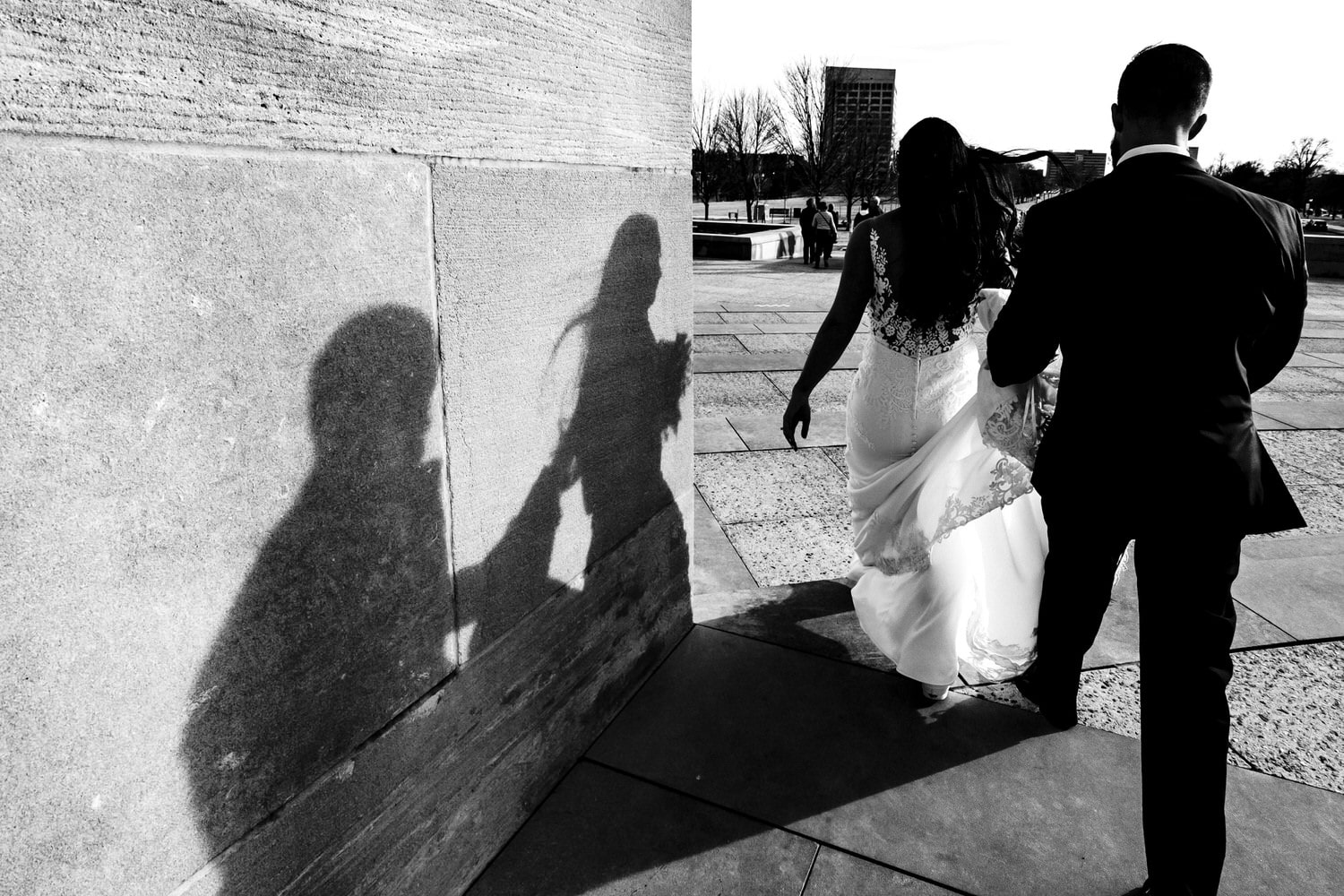A candid black and white picture of a bride and groom walking away from the camera, their shadows visible on a wall. 