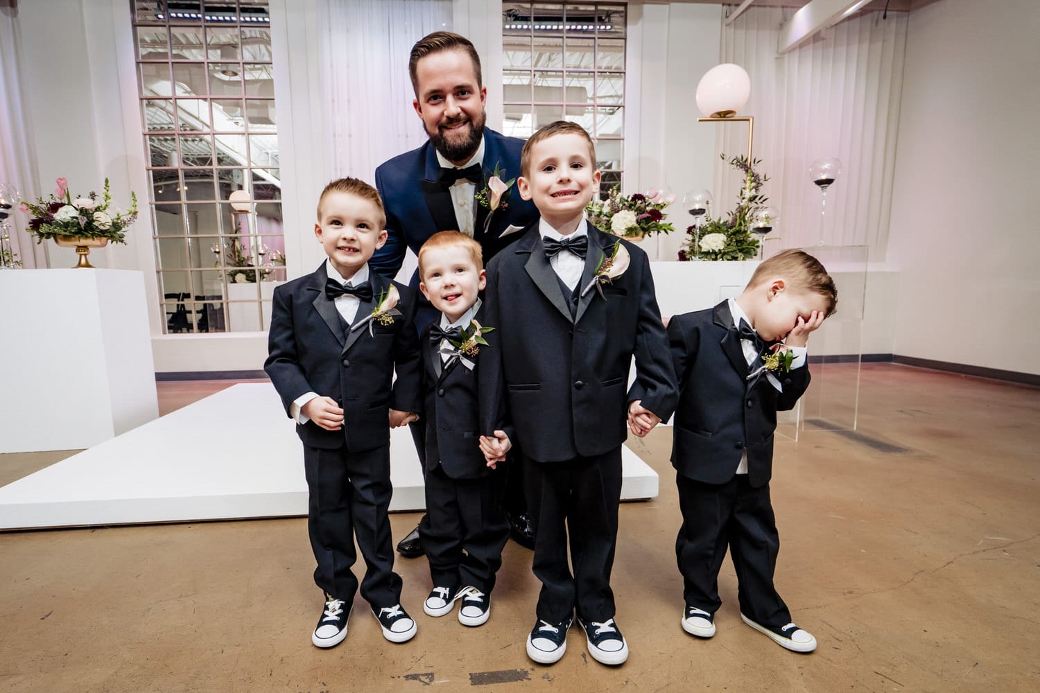 A colorful picture of four young ring bearers, one with his hand in his face, smiling for the camera with a groom on a winter wedding day at Pennway Place in Kansas City. 