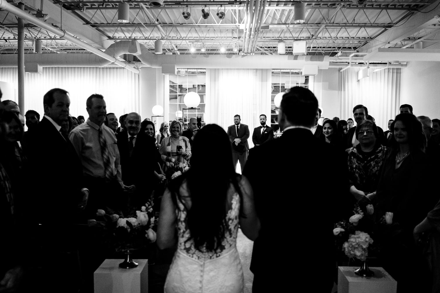 A candid black and white picture taken over the bride's shoulder of a groom waiting at the front of the aisle at Pennway Place by Studio Dan Meiners in Kansas City. 