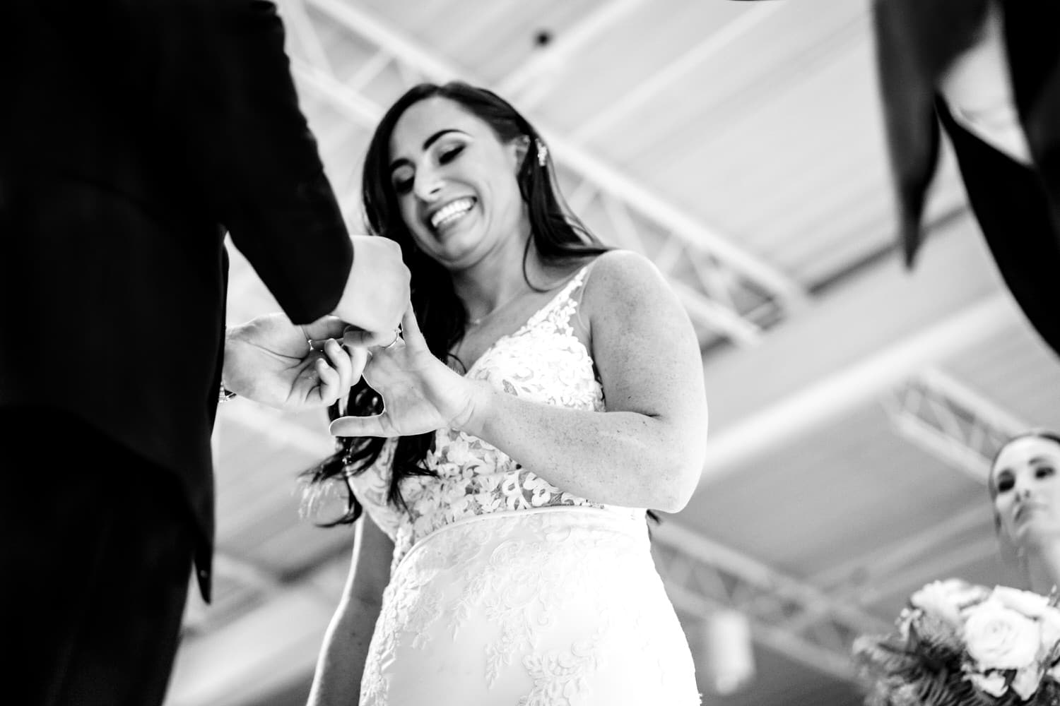 A candid black and white picture of a bride smiling at her groom as he puts a ring on her finger during their winter wedding ceremony at Pennway Place in Kansas City. 