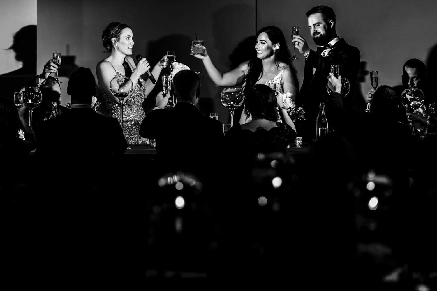 A black and white picture of a bride and groom toasting with their maid of honor during a wedding reception in Kansas City. 