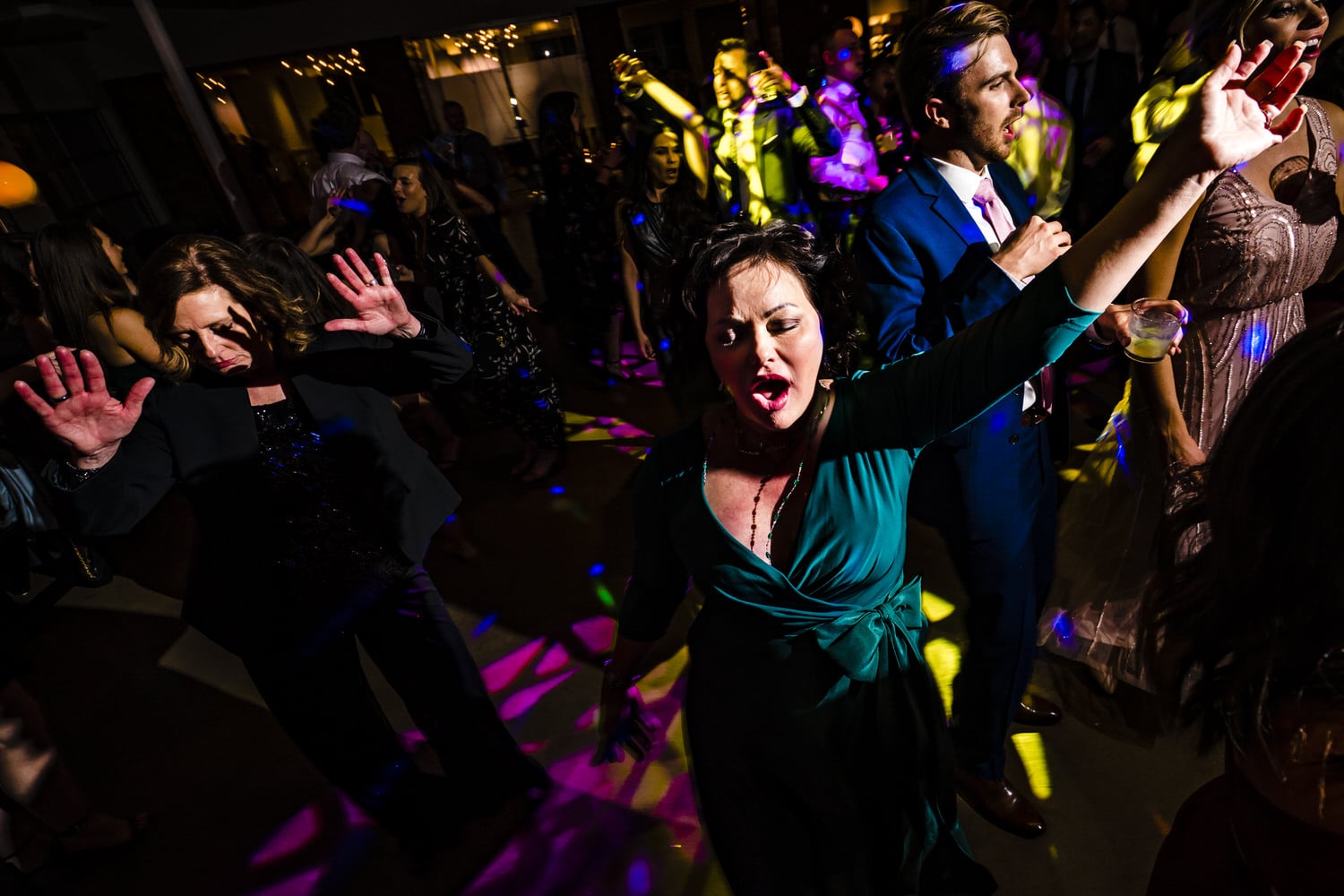 A candid picture of a woman in a green dress, arms outstretched singing along to the music during a wedding reception at Pennway Place in Kansas City. 
