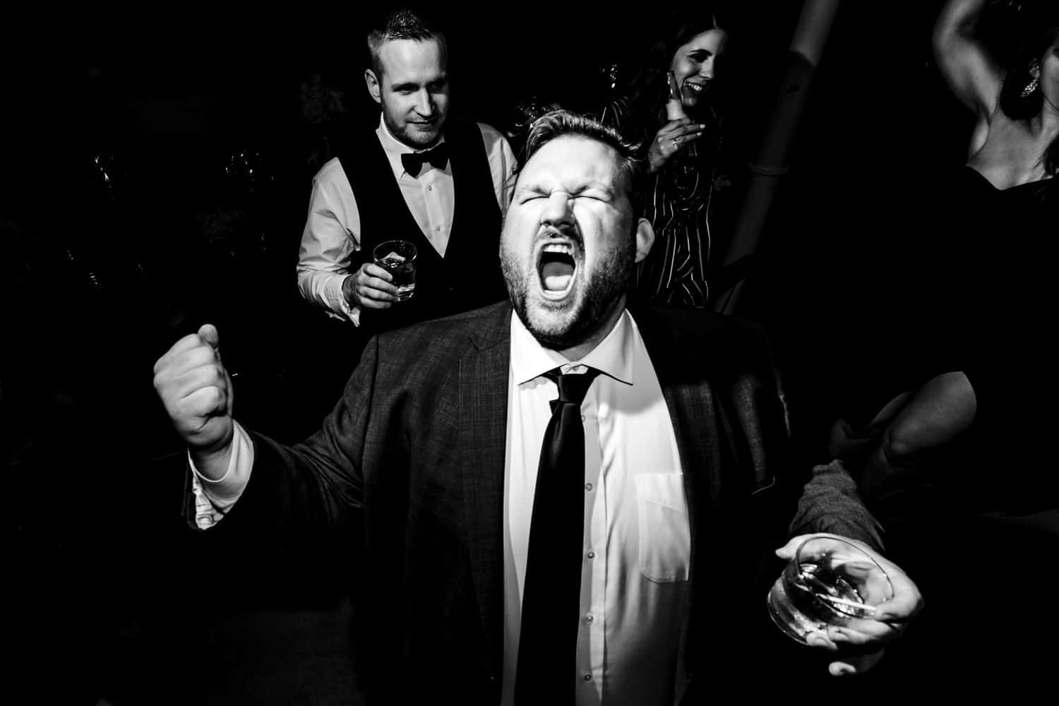 A candid black and white picture of a man in a suit screaming along to the music at a wedding reception in Kansas City at Pennway Place. 